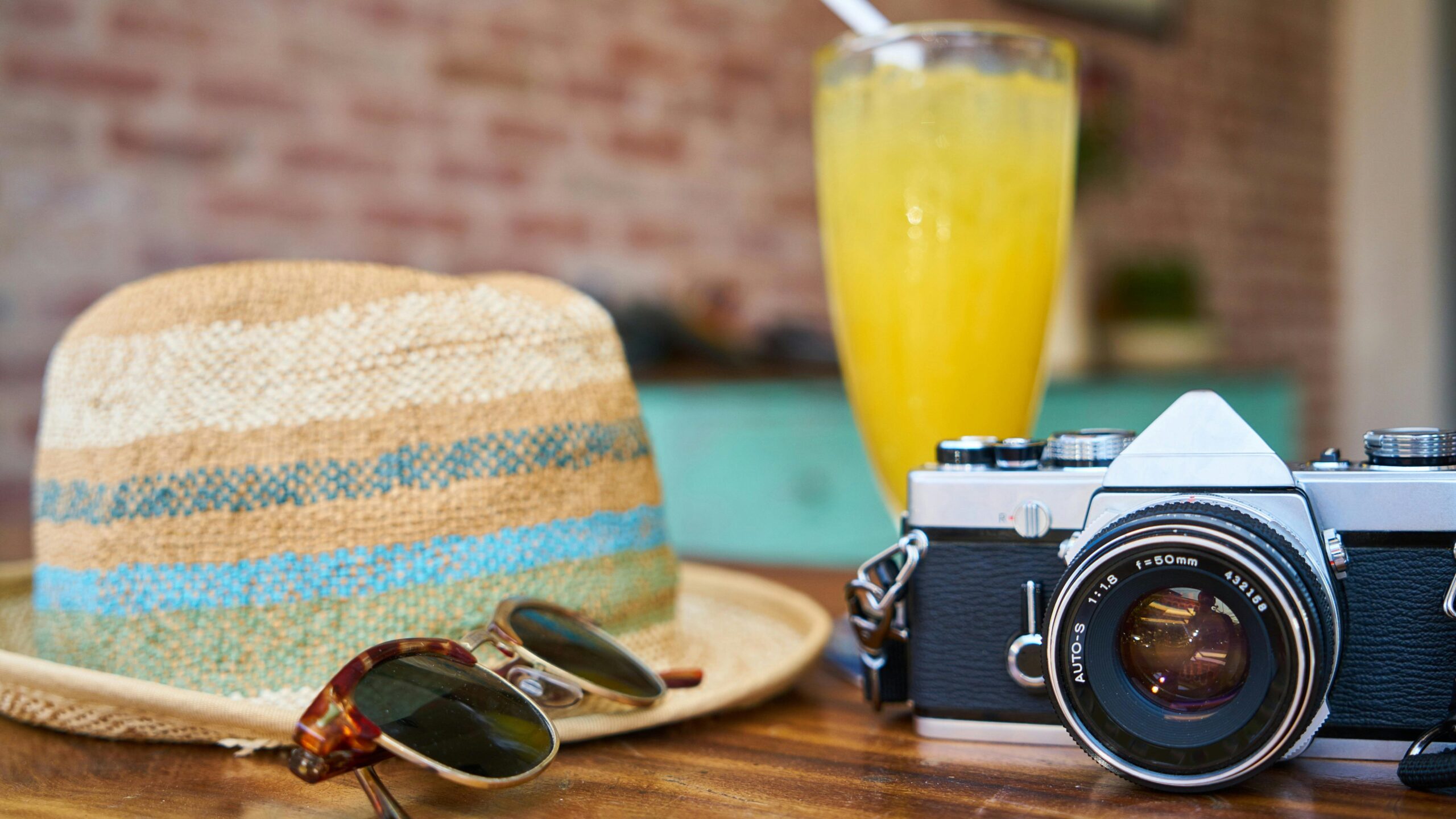 A stylish scene showcasing a vintage camera, hat, and orange juice, evoking summer travel vibes.